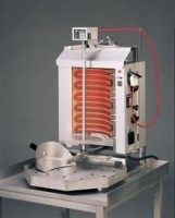 Das Bild zeigt das Gerät auf einem kleinen Edelstahltisch vor einem dunkegrauen Hintergrund. Das Geräte ist eingeschaltet, Das Bild zeigt das Gerät auf einem kleinen Edelstahltisch vor einem dunkegrauen Hintergrund. Das Geräte ist eingeschaltet, was an den rotglühenden Heizelementen zu erkennen ist. Die Perspektive ist schräg von vorne.